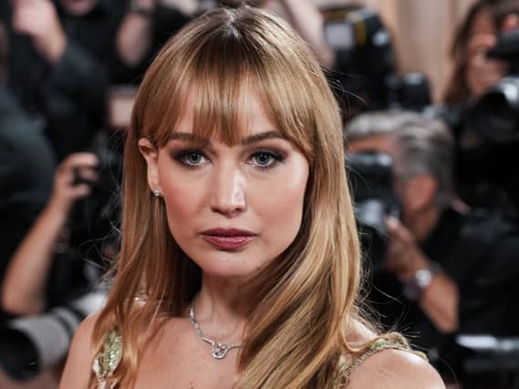 Headshot of Jennifer Lawrence posing for photos, with a bank of photographers behind her