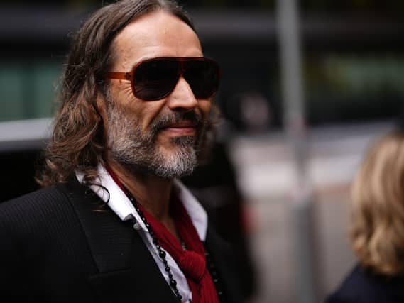 Russell Brand smiling while walking outside court, wearing sunglasses