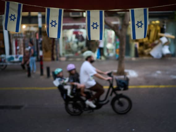 Israeli flags hang at a shop as a bicyclist carrying children passes by