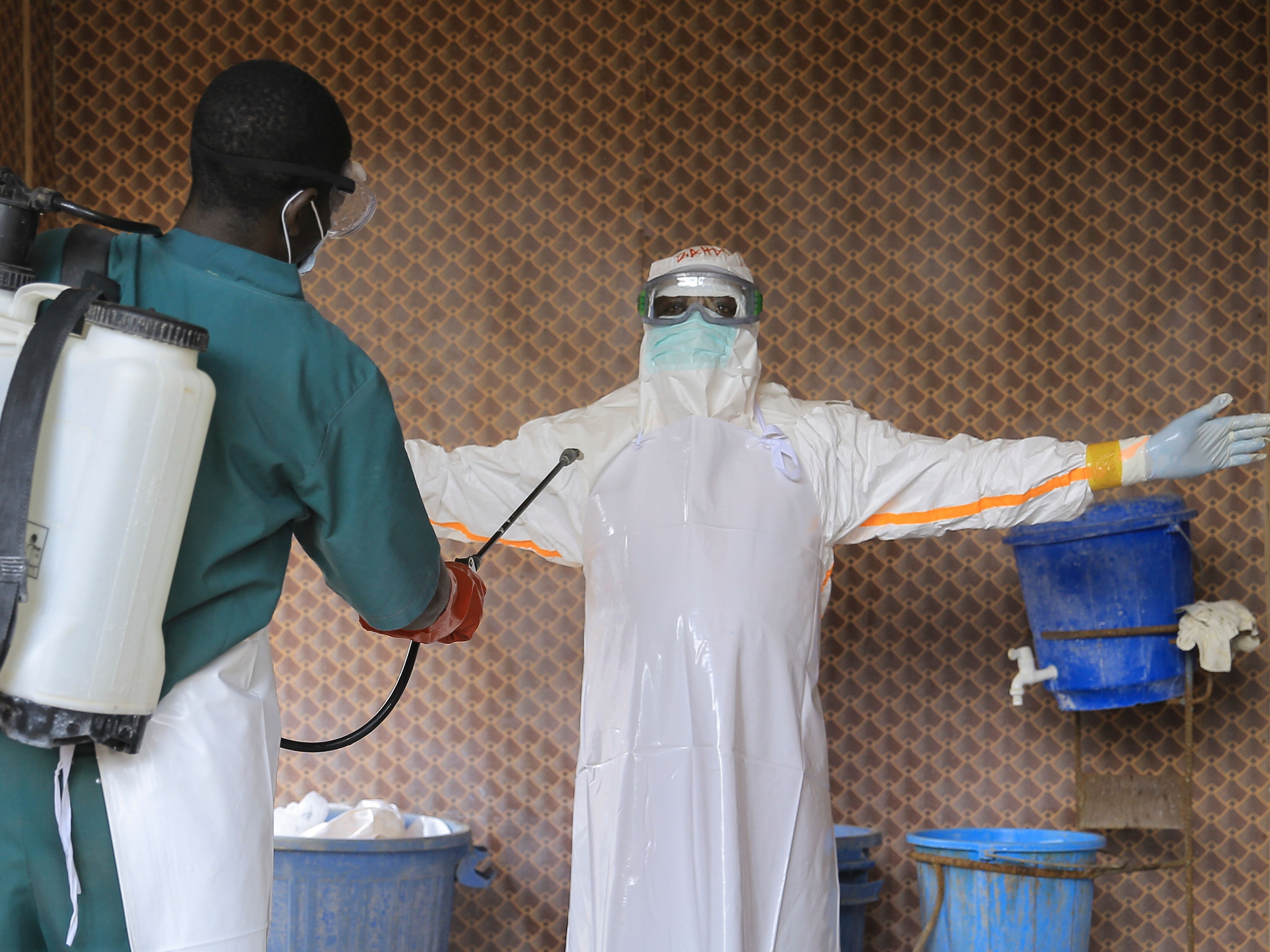 A healthcare worker in PPE being sprayed with a chemical