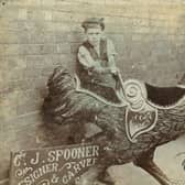 Historical photograph showing a young boy posing beside a carved fairground cockerel manufactured by C J Spooner