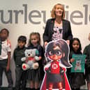 Children and adults pose together at Burleyfields Primary School alongside the school's display, with a teddy bear, book and superhero character cut-out.