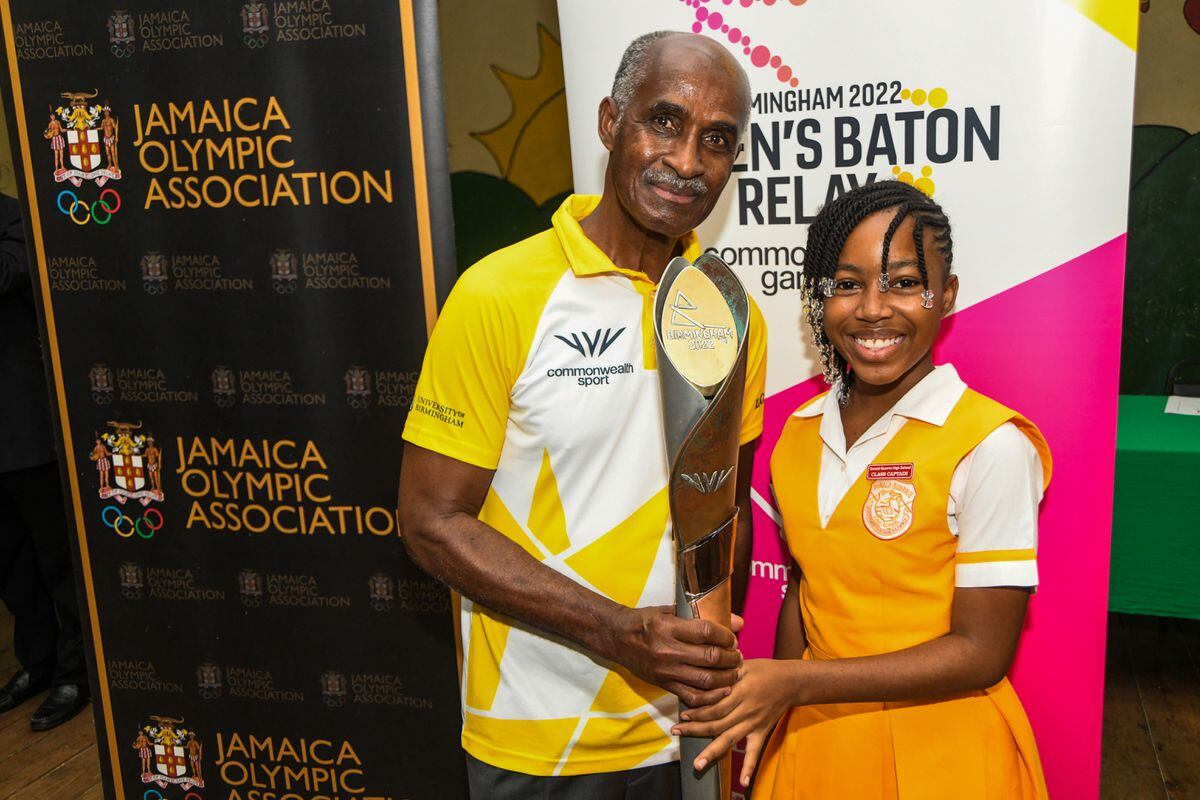 1976 Olympic gold medalist Don Quarrie holds the baton alongside a student in Jamaica