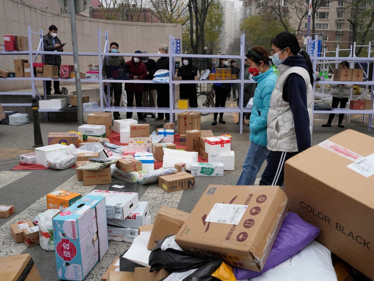 Residents wait for their deliveries behind shelves outside a community in Beijing
