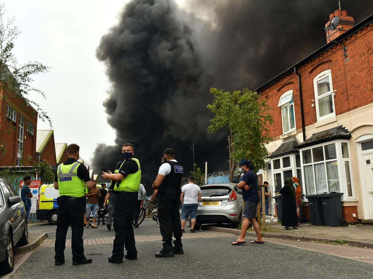 Police and local residents watch on as smoke billows from a severe blaze on an industrial estate in Birmingham