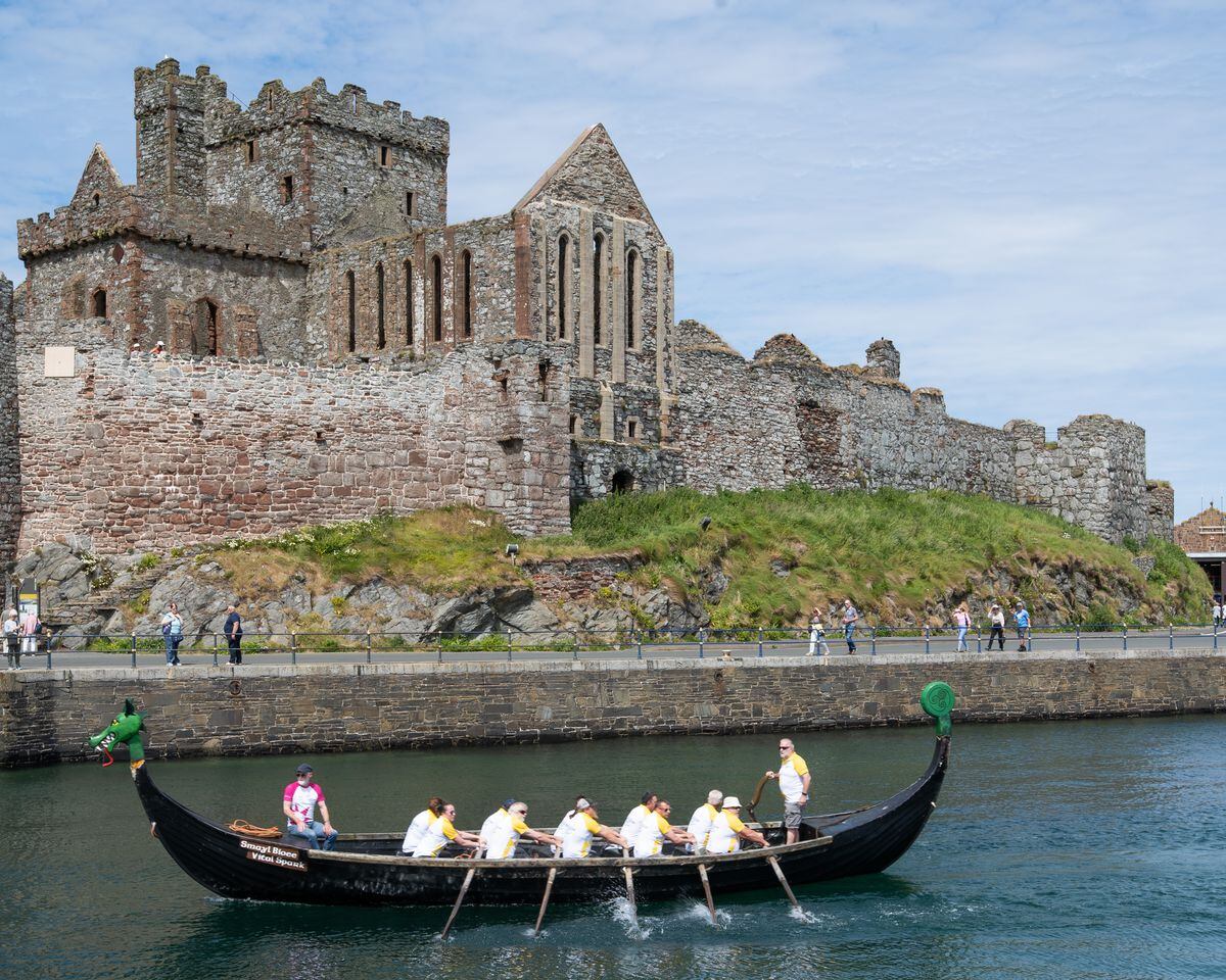 Baton-bearer aboard a Viking Long Boat sailing past Peel Castle, to meet the next baton-bearer in the Isle of Man