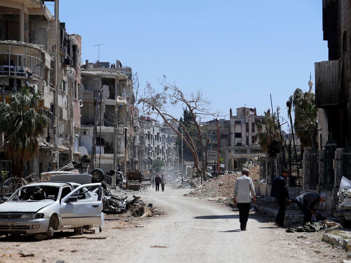 Syrians walk through destruction in Douma in April 2018