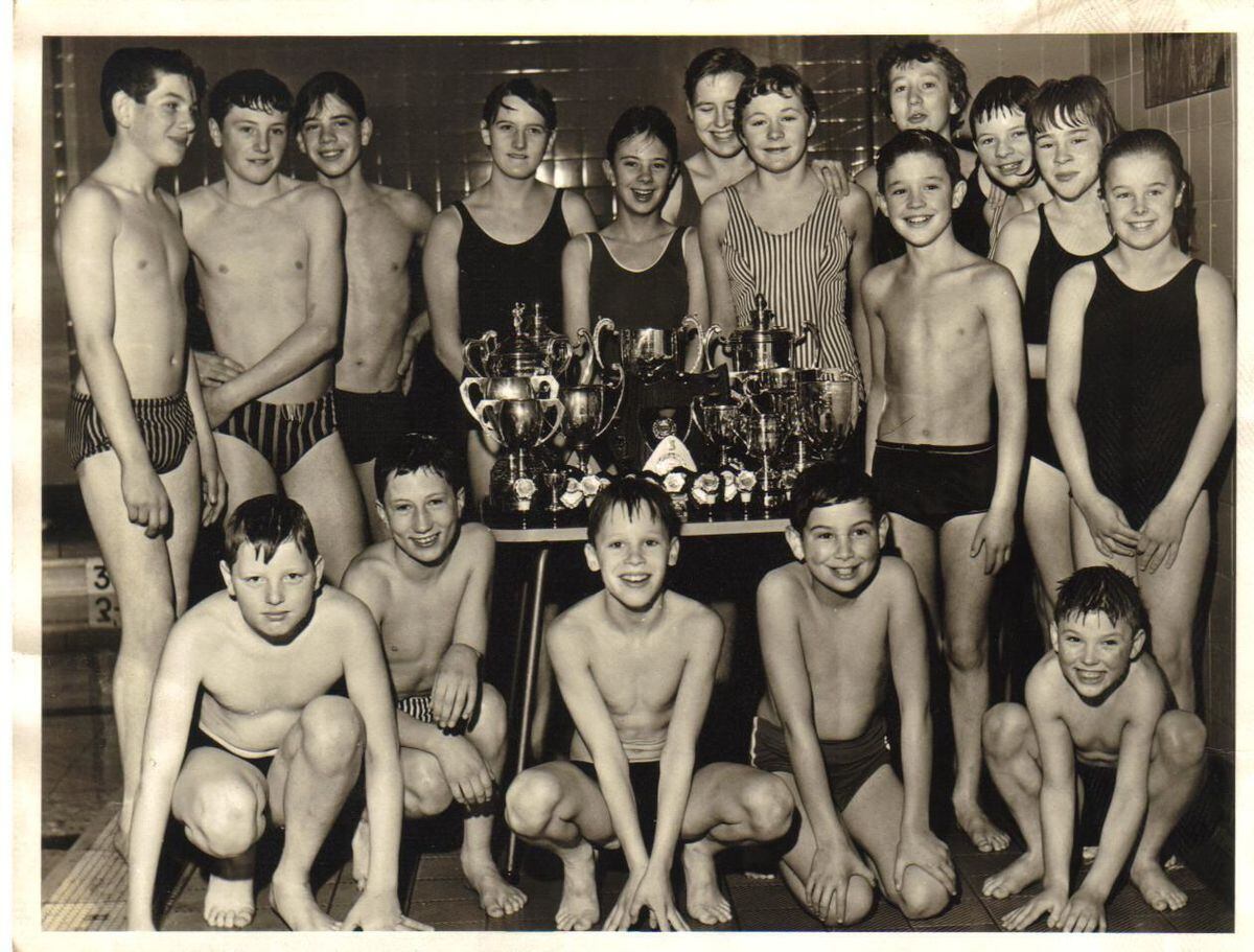 Brierley Hill Amateur Swimming Club members with their haul of trophies in December 1964: Back – Michael Dunn, Michael Palmer, Mike Overton, Irene Crombie, Lynne Ford, Ann Udall, Katie Tunnicliffe, Rosie Bowen, Liz Brown, Gayle Marklew, Carol Thatcher; next to table – Clive Davies; Front – John Howells, Chris Harris, Kevin Marklew, David Brown, Barry Davies.