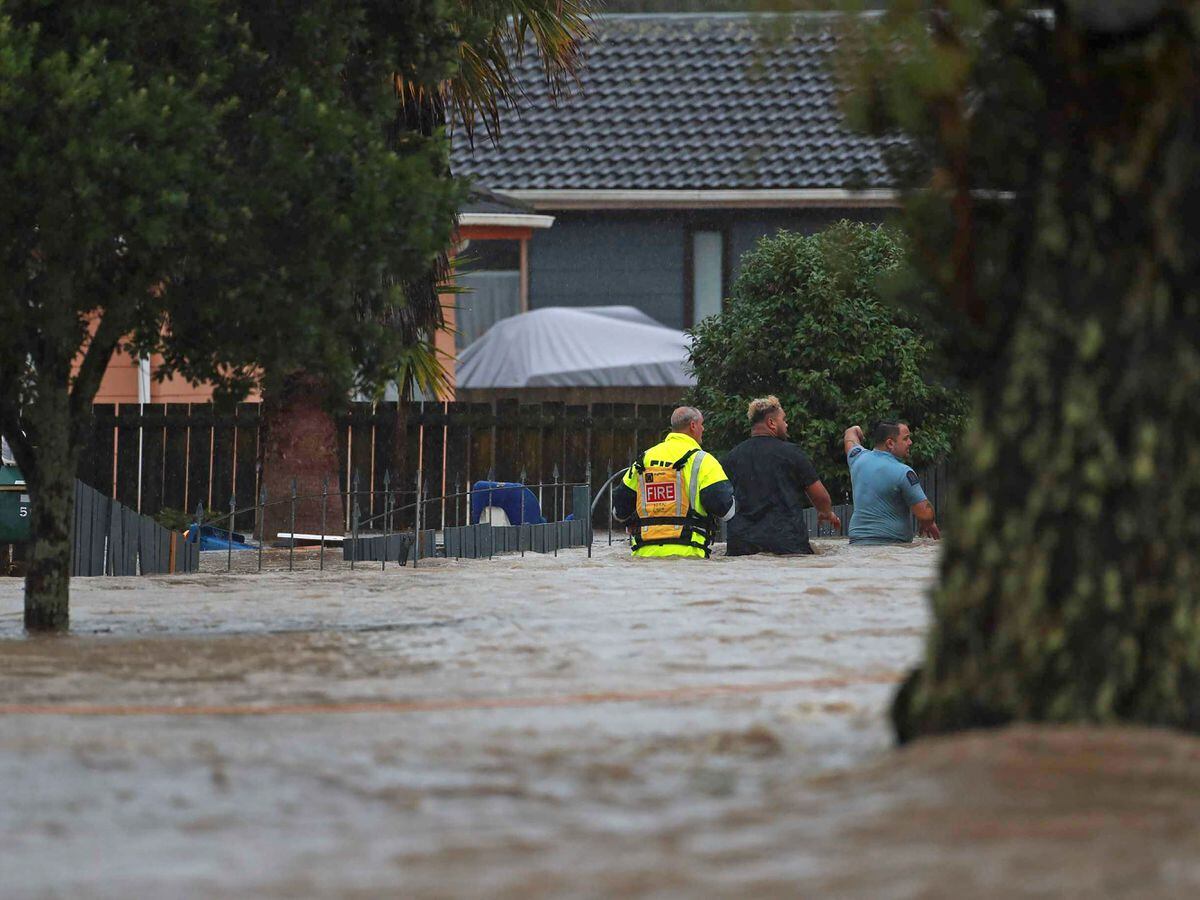 Emergency workers and a man wade through flood waters in Auckland, New Zealand, Friday, Jan. 27, 2023