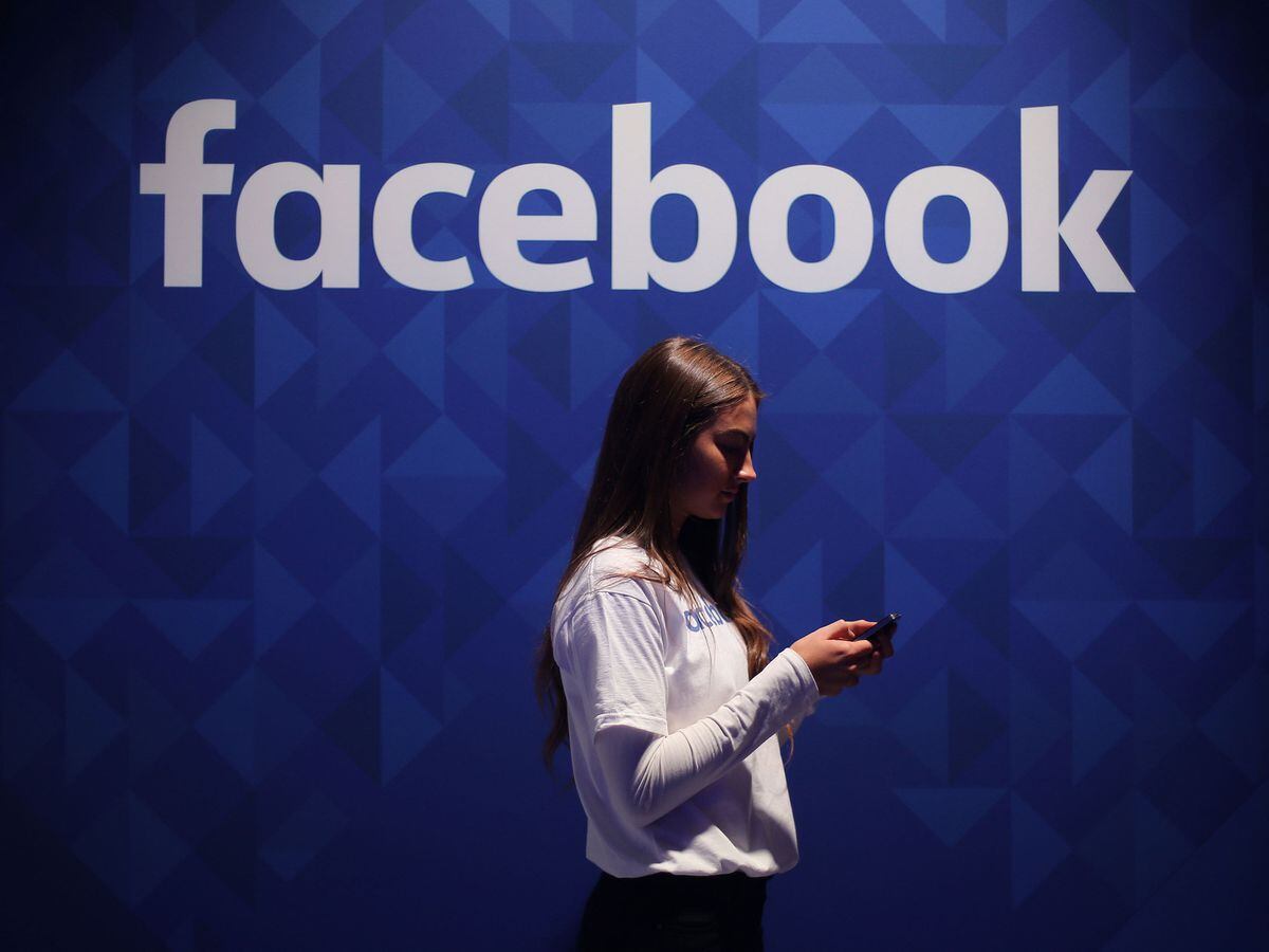 A woman uses her smartphone under a Facebook logo