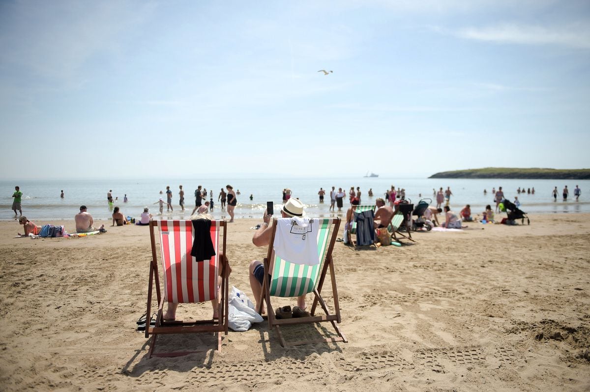 People relax in traditional deck chairs on the beach at Barry Island, South Wales