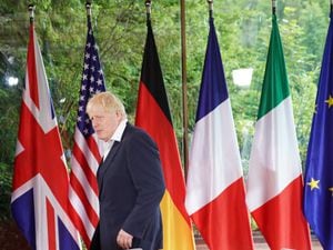 Boris Johnson walks in front of the G7 flags
