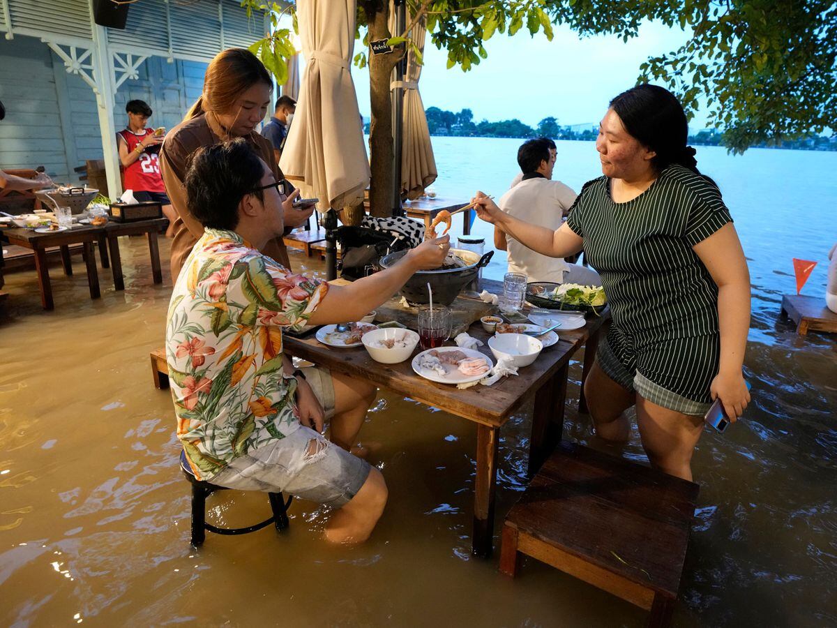 Les clients du Riverside Chaopraya Antique Cafe s'amusent malgré les niveaux d'eau élevés de la rivière Chao Phraya à Nonthaburi, près de Bangkok, Thaïlande