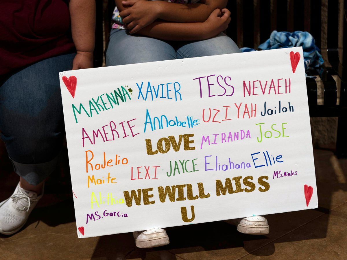 Stormy Flores, 11, sits with a sign bearing the names of the Robb Elementary School shooting victims