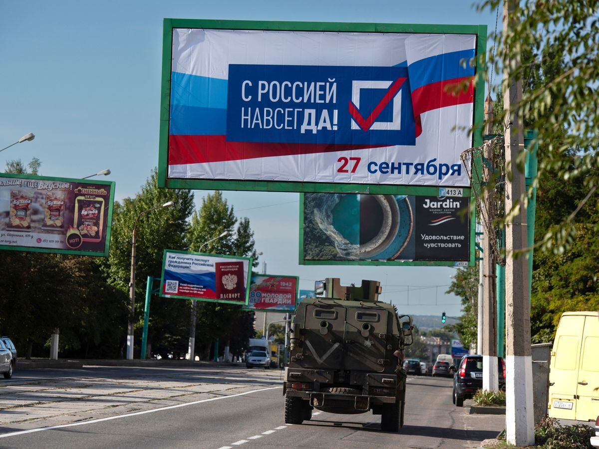 A military vehicle drives along a street with a billboard that reads: 'With Russia forever, September 27', prior to a referendum in Luhansk