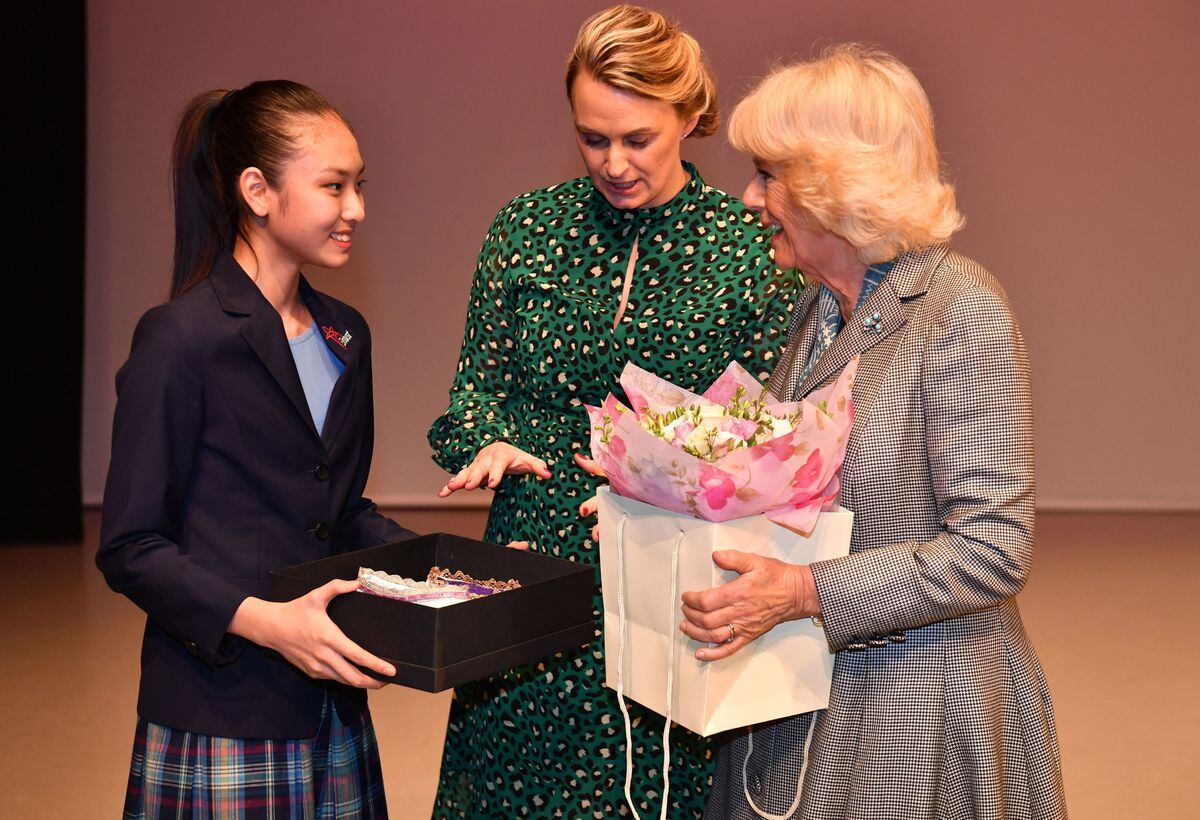 The Duchess of Cornwall receives a pair of ballet shoes from a pupil on stage during a visit to Elmhurst Ballet School