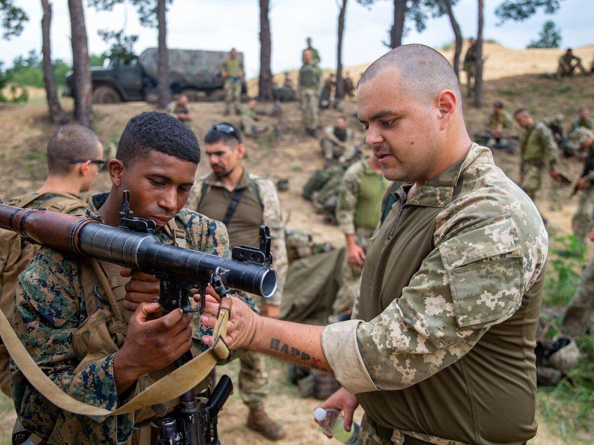 Aiden Aslin, a native of Nottingham, England and a rifleman with Air Assault Company, 1st Marine Battalion, 36th Naval Infantry Brigade, familiarizes U.S. Marine Corps Lance Cpl. Josef Mason, a native of New York City and a rifleman with Alpha Company, 1st Battalion, 6th Marine Regiment, 2d Marine Division, with an AK-74 assault rifle