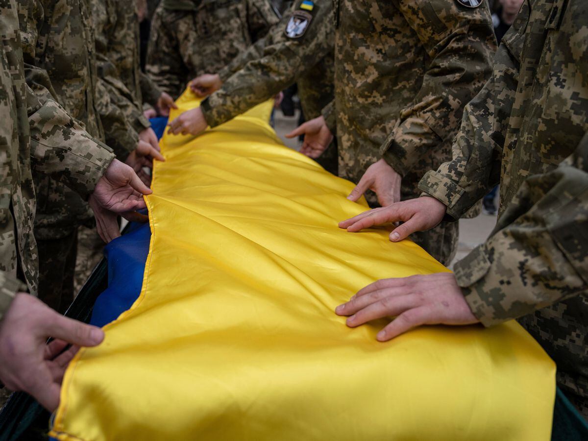 Ukrainian servicemen fold the national flag over the coffin of a comrade during a funeral