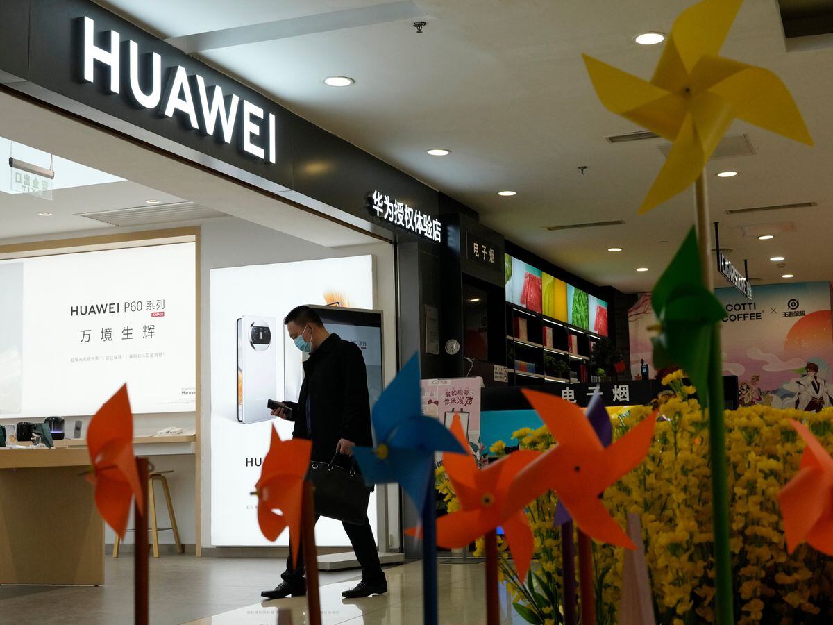 A man walks past a bed of plastic flowers outside the Huawei shop in Beijing