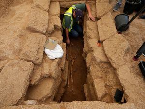 An archaeologist removes sand from a skeleton in a grave at the Roman cemetery