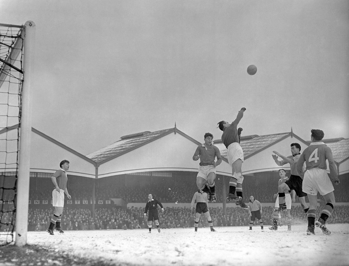 Manchester United goalkeeper Ray Wood and team mate Duncan Edwards, centre, jump high above the snow covered pitch to make a clearance from a Wolves attack spearheaded by centre forward Jimmy Murray (arms forward). Left, looking on is Manchester United's Bobby Charlton.