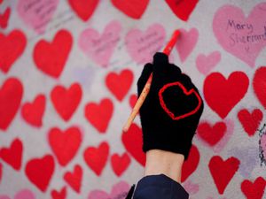 A volunteer from the Covid-19 Bereaved Families for Justice campaign group paints a heart on the National Covid Memorial Wall opposite the Palace of Westminster in central London (Victoria Jones/PA)