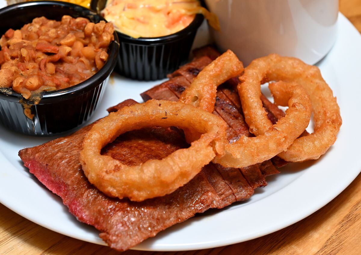 The steak after it's been cooked and plated up with onion rings, mushroom, fries and corn
