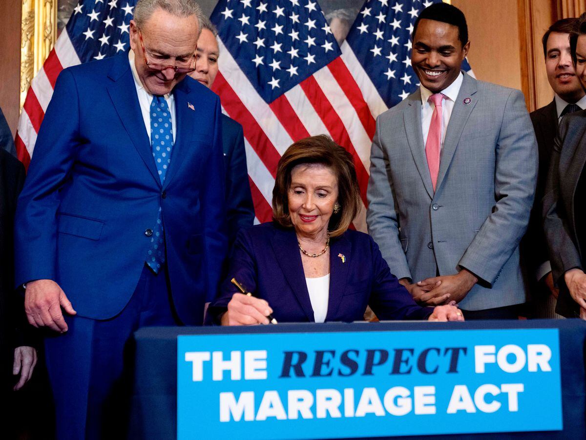 House Speaker Nancy Pelosi of Calif., accompanied by Senate Majority Leader Sen. Chuck Schumer of N.Y., left, and other members of Congress, signs the H.R. 8404, the Respect For Marriage Act