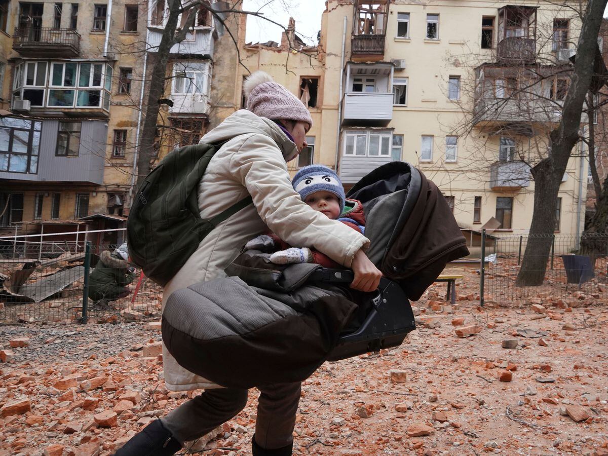 A woman carries her child as they evacuate from a residential building which was hit by a Russian rocket at the city centre of Kharkiv, Ukraine