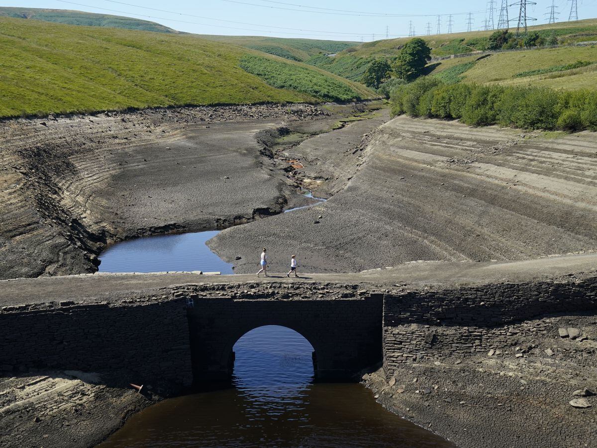 People walk across the dry cracked earth at Baitings Reservoir in Ripponden, West Yorkshire, where water levels are significantly low