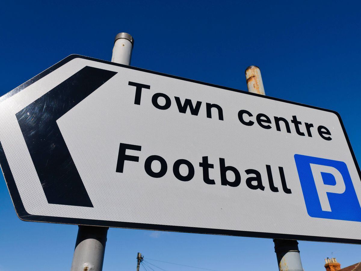 A road sign directing people to a town centre, and parking for a football stadium