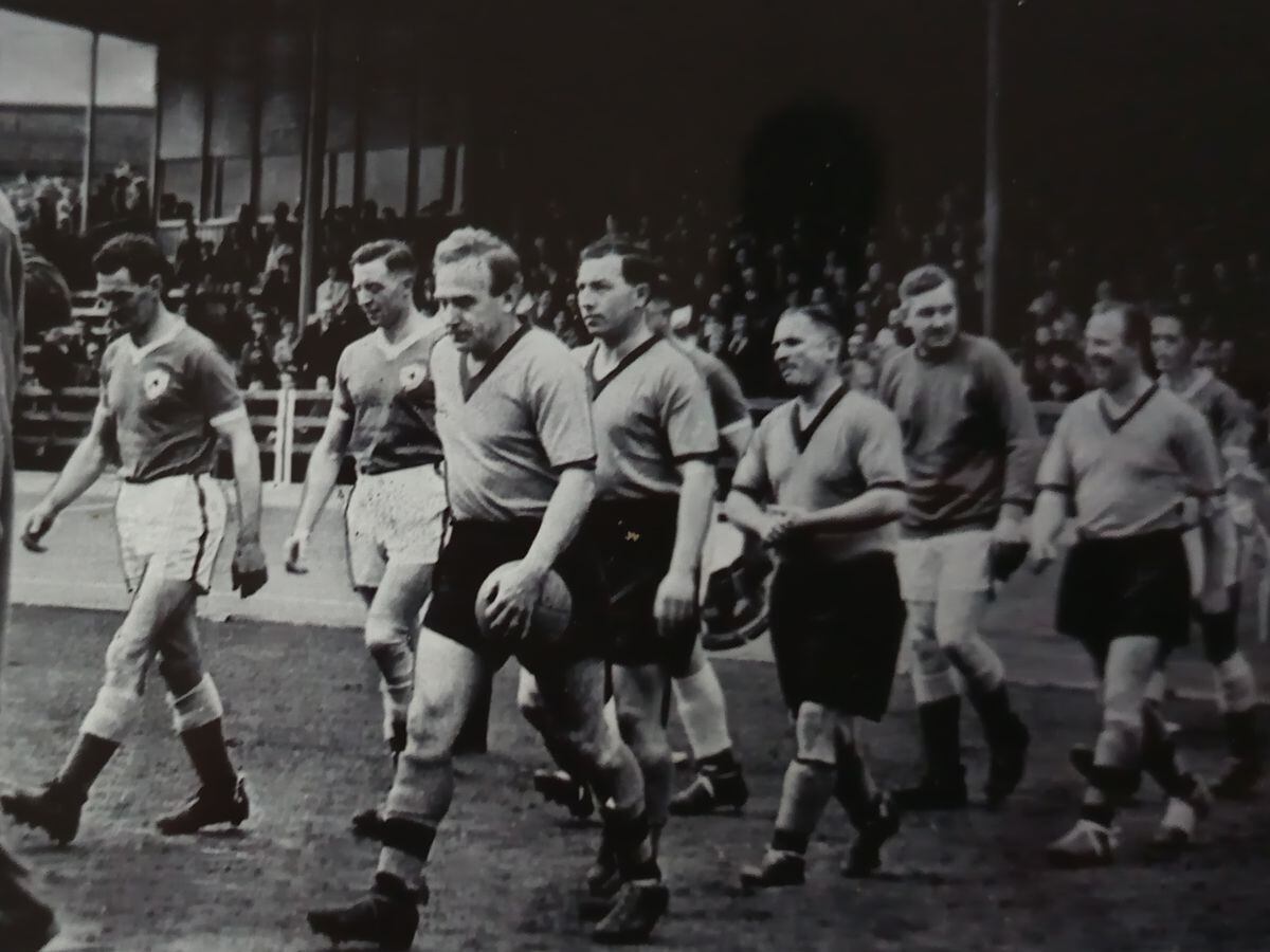 Frank Knowles, in light coat, walks behind Wolves manager Stan Cullis as captain Billy Wright leads the Wolves team out in a charity football match against Leicester at Aldersley Stadium in 1949